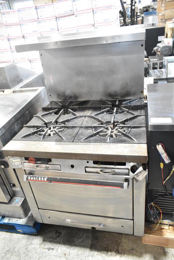 Garland commercial 4-burner gas range with oven, over-shelf, and back splash. Used condition, visible Garland branding.