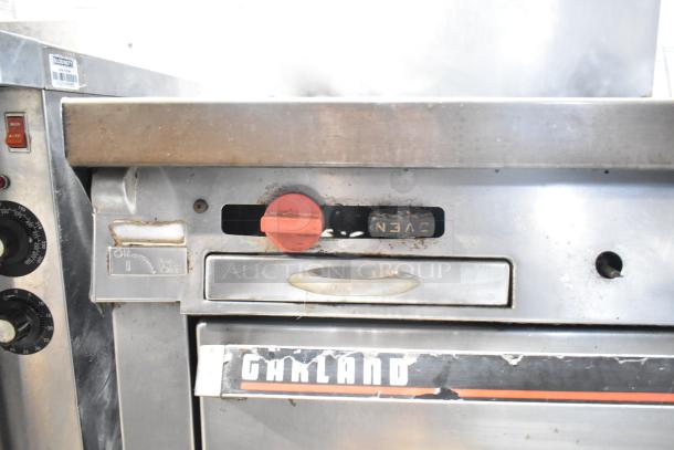 Garland commercial gas-powered 4 burner range with oven, over shelf, back splash. Visible branding and control knobs, used condition.