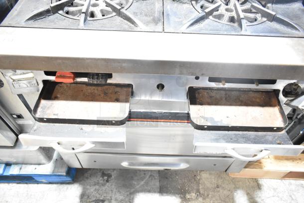 Garland commercial gas range with 4 burners, oven, over shelf, and back splash. Visible wear on drip trays.