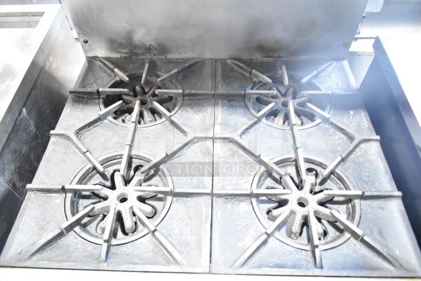 Garland commercial gas-powered 4 burner range, featuring oven, over shelf, and backsplash. Condition shows signs of use.