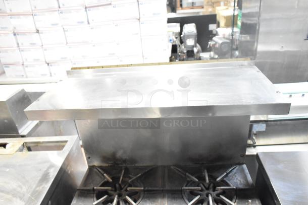 Garland commercial gas-powered 4 burner range with oven, over shelf, and backsplash. Durable steel, moderate wear.