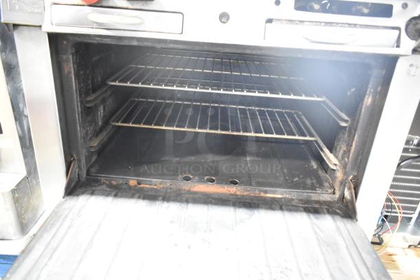 Garland commercial gas 4 burner range with oven, over shelf, and backsplash. Interior shows use; solid build, functional.