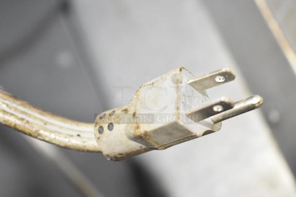 White electrical plug with three prongs, slightly worn and showing signs of use, attached to a metal cable.