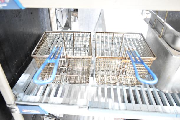Two fryer baskets with blue handles on a metal rack, part of a set including two fryer drop-in bins. Used condition.