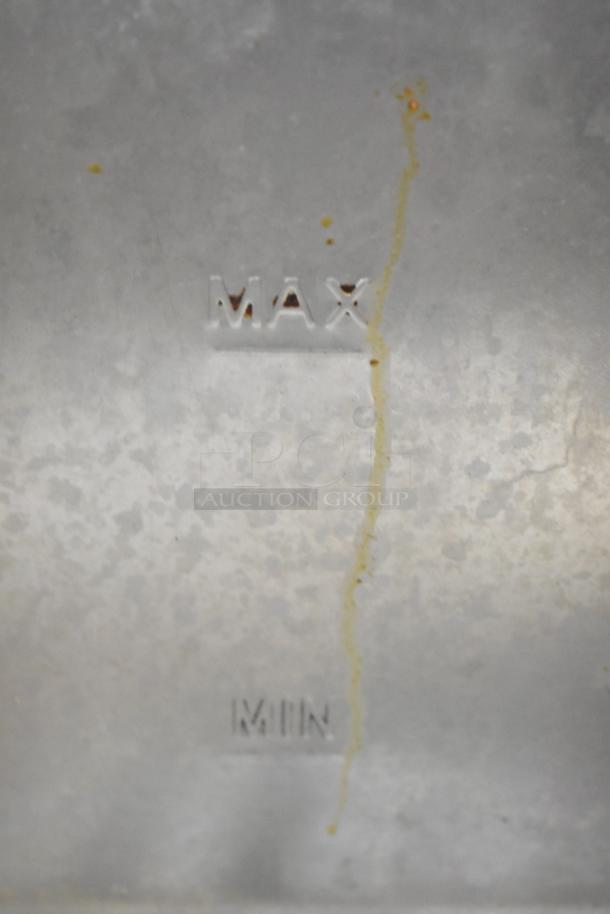 Stainless fryer drop-in bin with visible max and min markings, showing slight wear with oil residue.