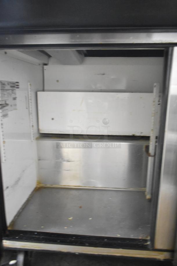 True TSSU-72-30M-B-ST commercial sandwich prep table interior view, shows used condition; shelves and labeling visible.