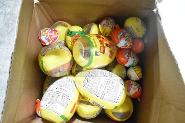 Box of candy including Kinder Joy eggs, visible labels with nutritional information. Variety of flavors inside.