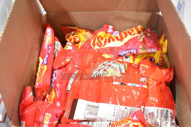 Box filled with assorted candy packs including KitKats, Starburst, and more, showcasing colorful packaging and variety.