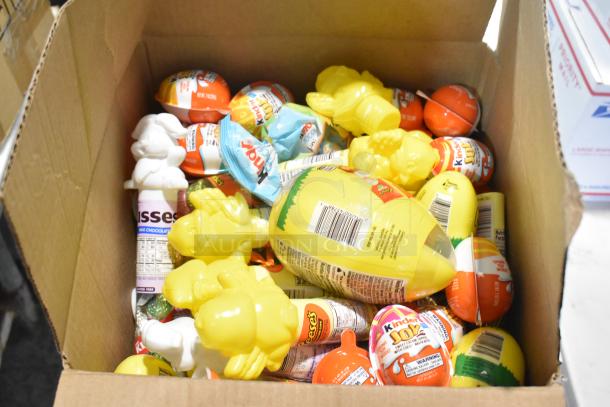 Box filled with assorted candies including Kinder Joy, Reese’s, and yellow chocolate bunnies. Includes various packaging.