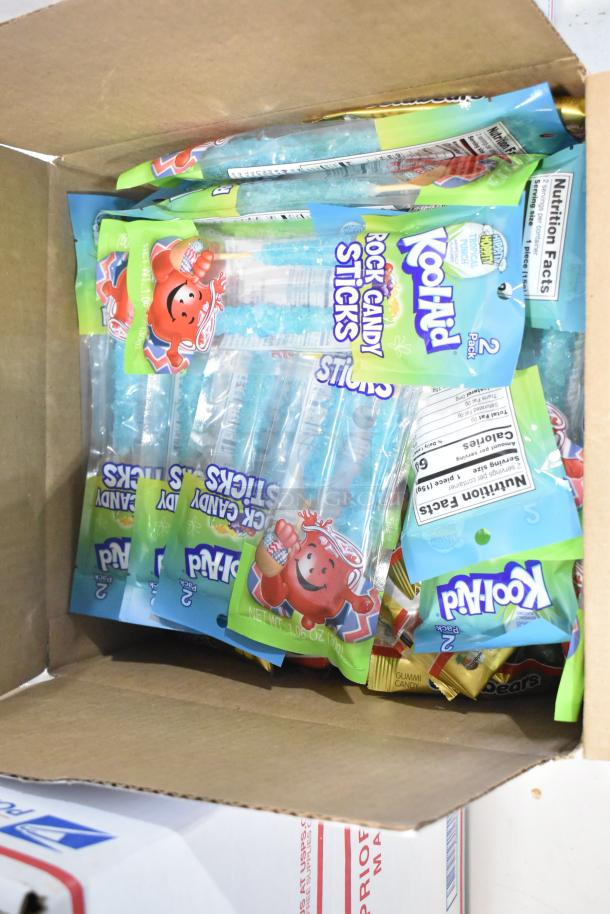Box containing Kool-Aid Rock Candy Sticks, part of an auction lot with 10 boxes of various candies including marshmallows, chocolate, and gummies.