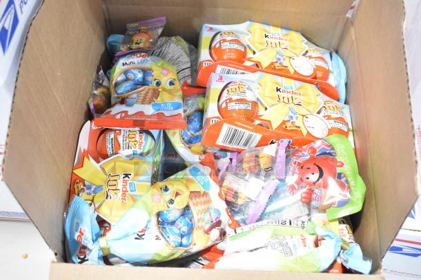 Box of assorted candies, including Kinder Joy eggs. Various colorful packaging visible. Perfect for candy lovers.