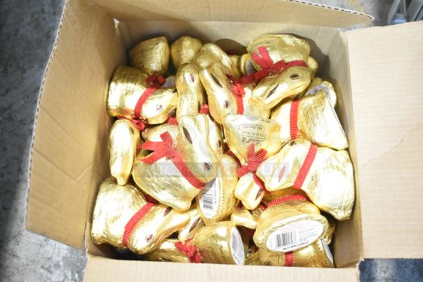 Cardboard box containing multiple gold foil-wrapped chocolate bunnies with red ribbons, tagged as Lindt Gold Bunny.
