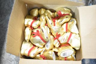Cardboard box containing multiple gold foil-wrapped chocolate bunnies with red ribbons, tagged as Lindt Gold Bunny.