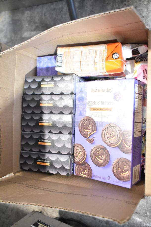 Box containing 10 boxes of candy including Mamba Berrytastic, Lindt Lindor, Russell Stover eggs, and treats like jack-o'-lantern cookies and Moonlit Cottage kits.