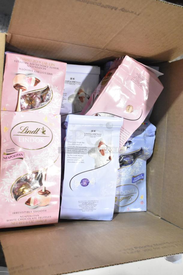 Ten boxes of assorted candies including Lindt Lindor Neapolitan White Chocolate Truffles, visible in an open carton.