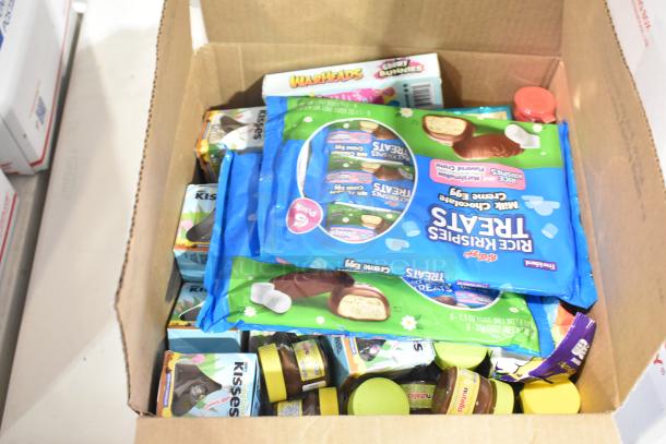 Cardboard box filled with various candy brands including Warheads Chewy Bunnies and Kellogg's Rice Krispies Treats packs.
