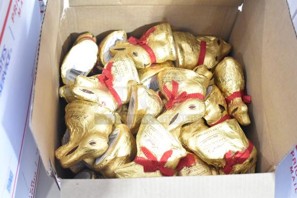 Box filled with gold foil-wrapped chocolate bunnies, featuring red ribbon collars and labeling indicating Lindt Gold Bunny.