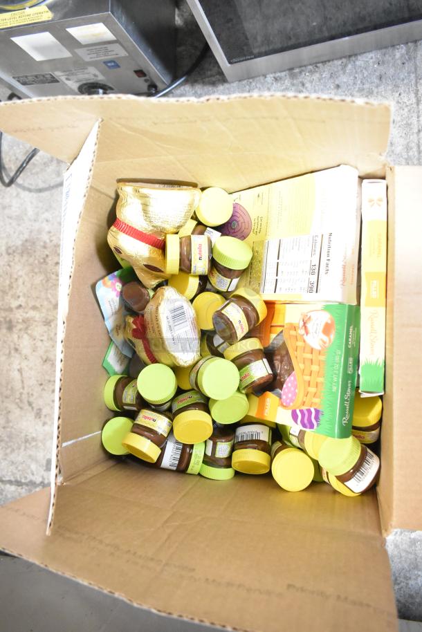 Auction item: Box with mini Nutella jars, gold foil chocolate bunnies, and assorted candy packets. Vibrant, unopened packaging.