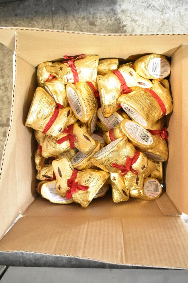 A box filled with Lindt Gold Bunny chocolate figurines, wrapped in gold foil with red ribbons.