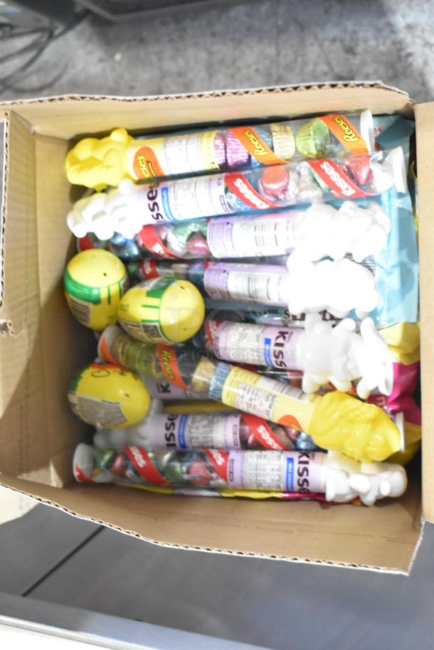 Cardboard box filled with Reese's and Hershey's candy tubes, Easter-themed chocolates, and yellow plastic eggs.