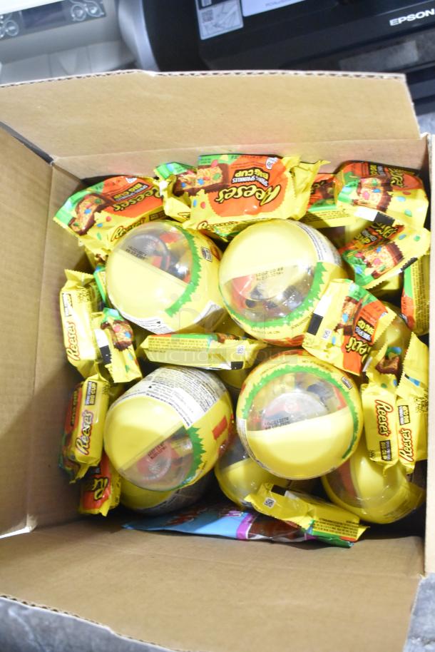 Box containing assorted candy, including Reese's Big Cup and sealed yellow containers. Items appear in good condition.