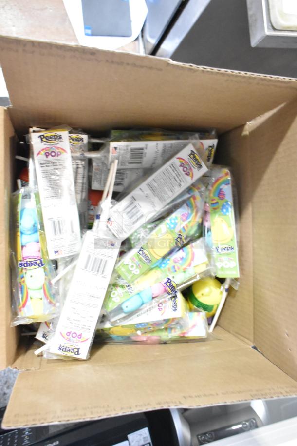 Open box containing various candy, including Peeps Pops in sealed packages, stacked and ready for auction, in new condition.