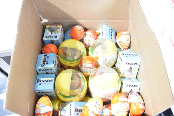 Boxes of various candies including Junior Mints, Kinder Joy Eggs, yellow Peeps, and Hershey's Kisses in a cardboard box.