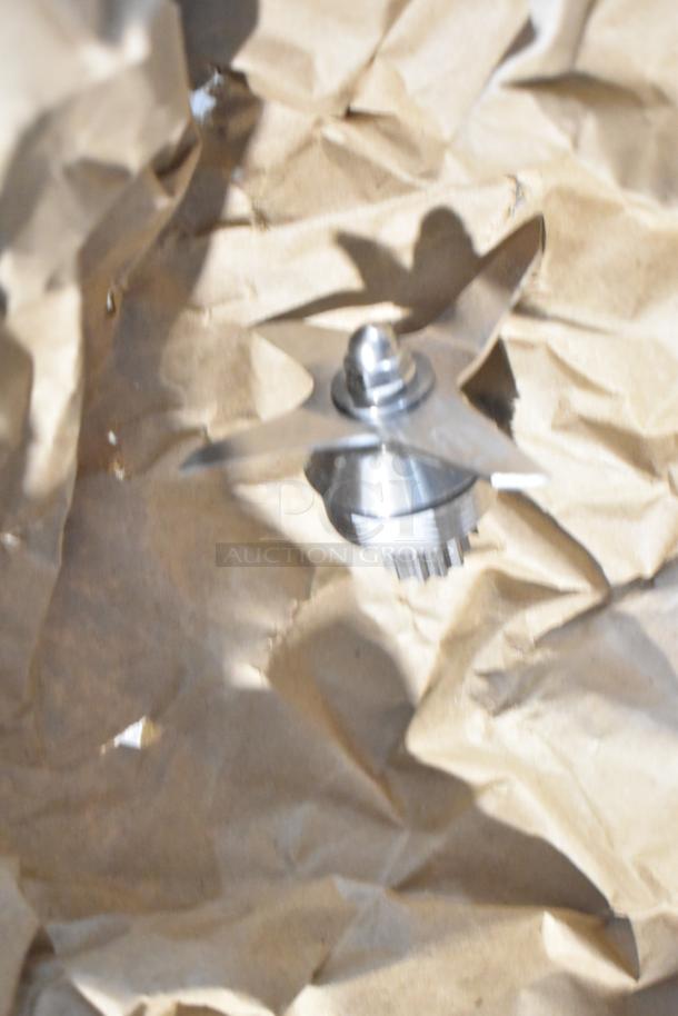 Stainless steel blender blade attachment on crumpled brown paper.