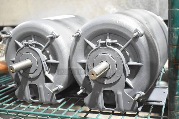 Two industrial motors, steel gray, mounted on a metal shelf. Both in good condition, feature exposed shafts.
