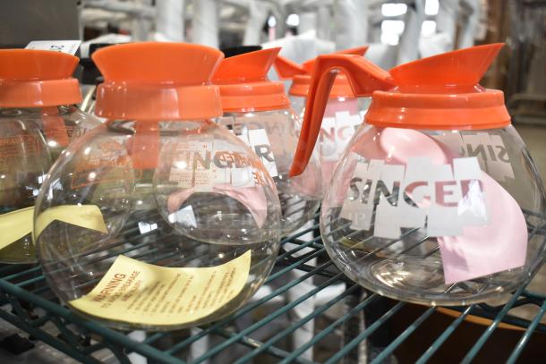 Nine brand new scratch and dent coffee pots with orange lids, various conditions, visible warning labels inside.