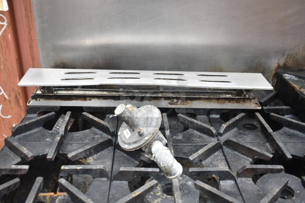 Commercial gas-powered 12 burner range featuring two ovens, over shelf, backsplash, on commercial casters. Moderate wear.