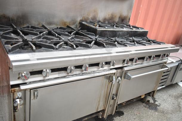 Commercial gas-powered 12-burner range with two ovens, over-shelf, backsplash, and commercial casters, showing wear.