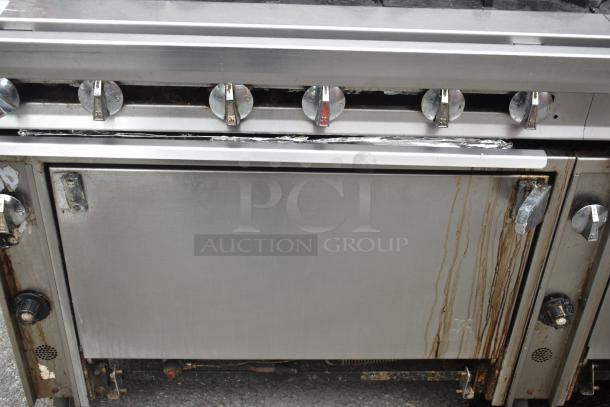 Commercial gas-powered 12-burner range with 2 ovens, over shelf, backsplash, and on casters. Used condition.