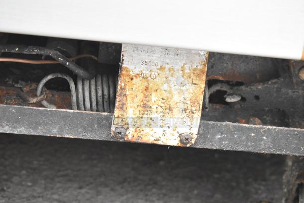 Rusty metal plate with faded text showing model and burner specifications, attached to a commercial rang.