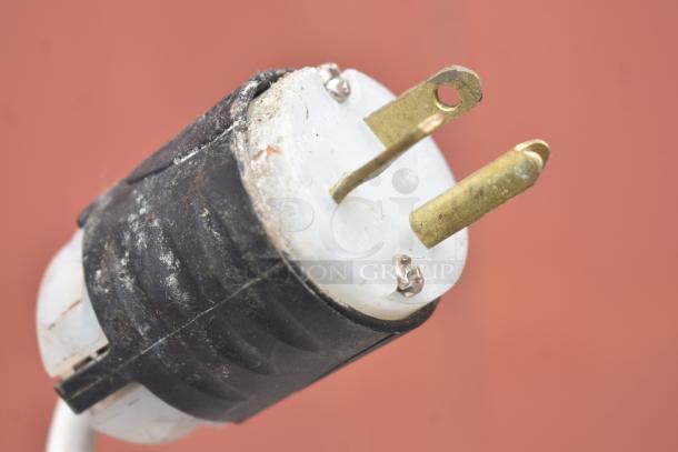Close-up of a weathered 208-volt electrical plug, showing brass prongs and a black rubber casing.