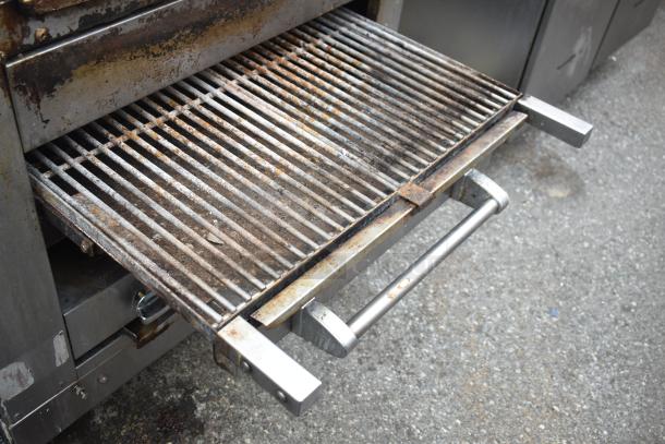 Commercial gas-powered vertical upright broiler with worn grill, stainless steel exterior, and mounted on commercial casters.