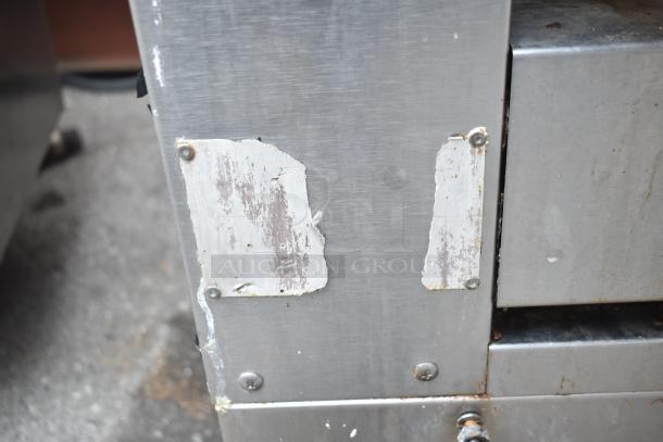 Commercial gas-powered vertical upright broiler on casters, stainless steel, visible wear, missing labels, industrial use.