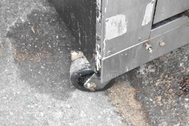 Commercial gas-powered vertical upright broiler on casters, showing wear, metal surface details, and robust wheels.