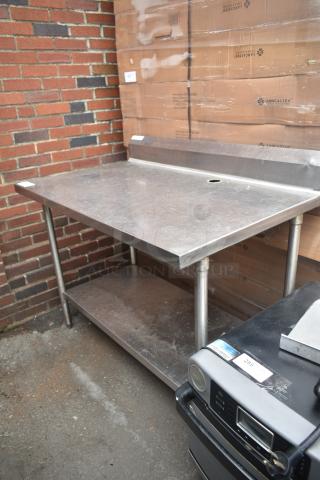 Stainless steel table with back splash, under shelf, and drain hole, in good condition, suitable for kitchen or industrial use.