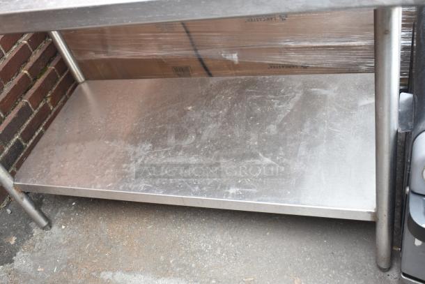 Stainless steel table with back splash and under shelf, showing signs of use.