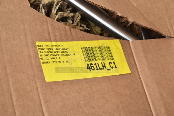 Cardboard box with yellow label, barcode, and text indicating Grand-Trunk Hospitality, Jersey City, NJ. Contains metal racks.