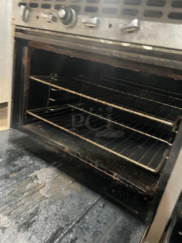 Bakers Pride stainless steel 10-burner gas range with double oven, backsplash, salamander shelf, and wired oven rack. Moderate wear.