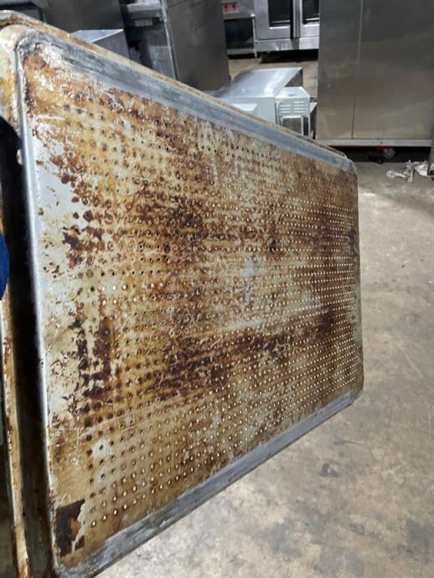 Commercial perforated sheet pan with heavy wear and rust. Ideal for baking; shows extensive use. Industrial setting background.