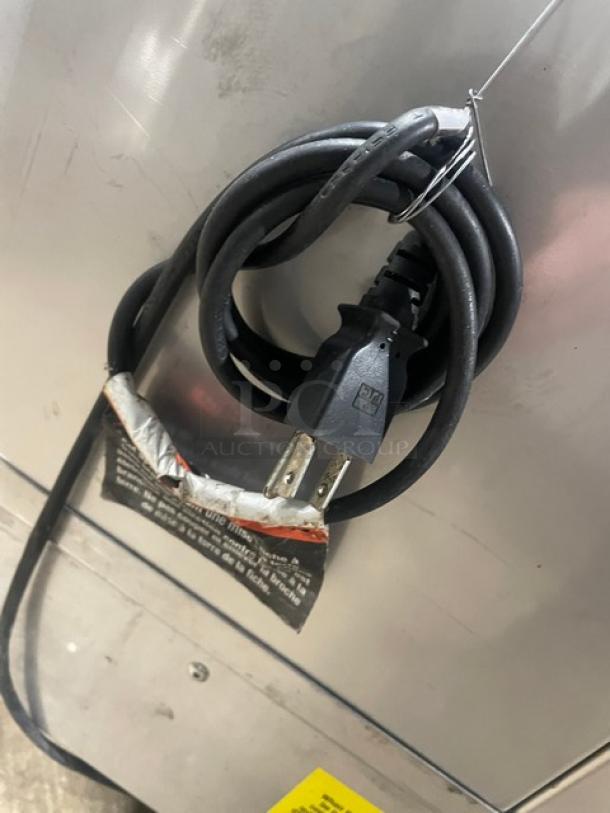 Coiled power cord with plug attached to a commercial stainless steel appliance, label partially visible.