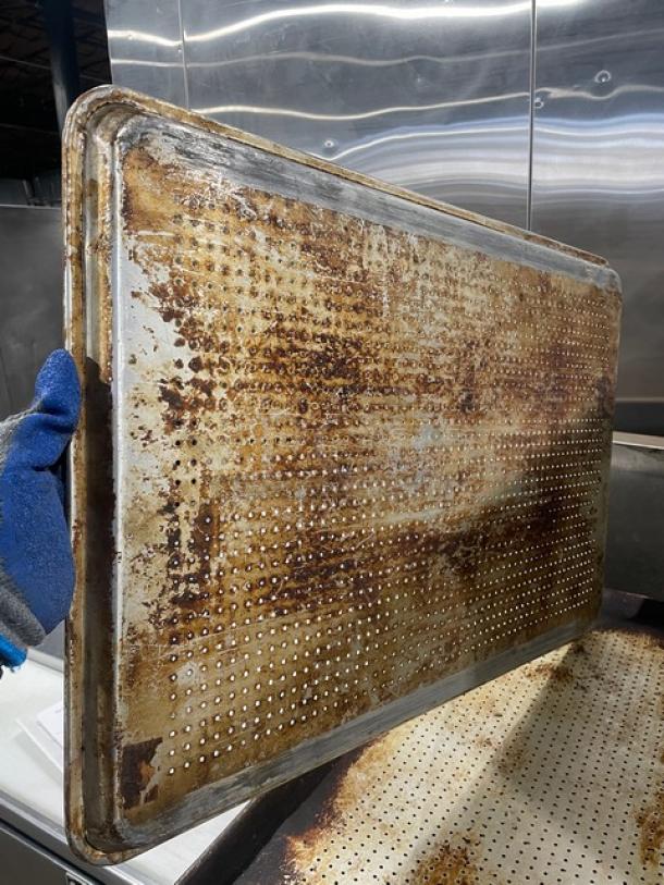Commercial perforated sheet pan, used condition, visible wear and patina, perforations for even baking.