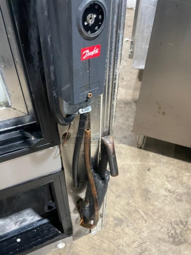 Commercial stainless steel curved glass bakery display case with multi-tier shelves and rear sliding glass doors. Visible Danfoss control panel.