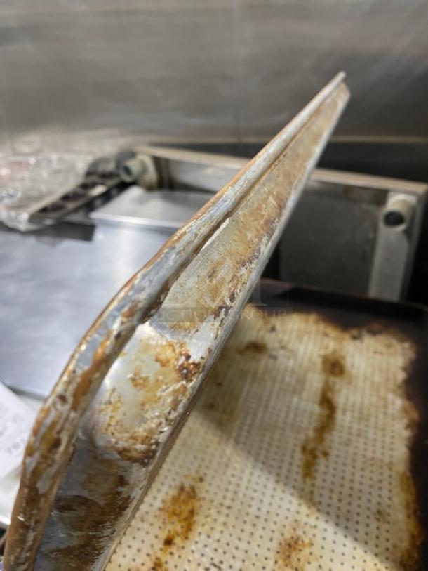 Commercial perforated sheet pan, metal, shows signs of use with rust spots, suitable for baking applications.