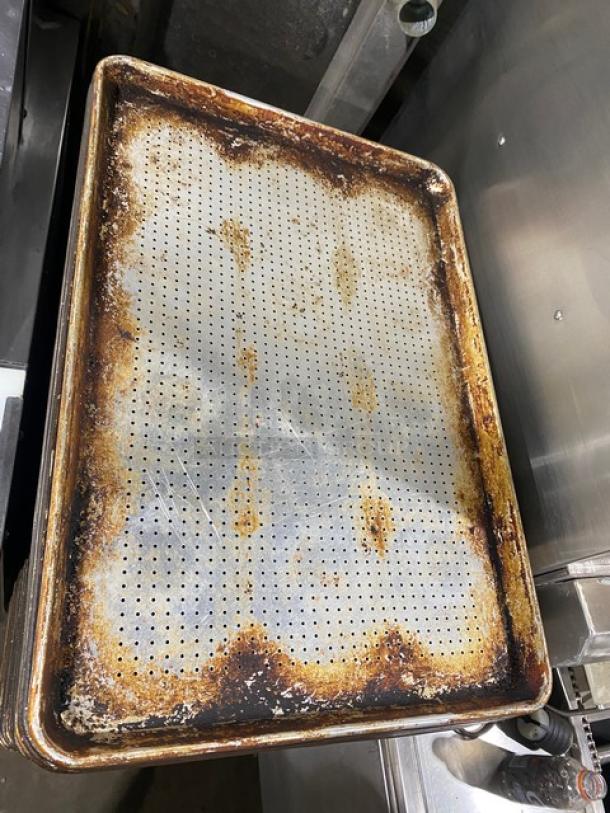 Commercial perforated sheet pan with visible wear and rust, used condition. Ideal for baking, auction includes five pans.