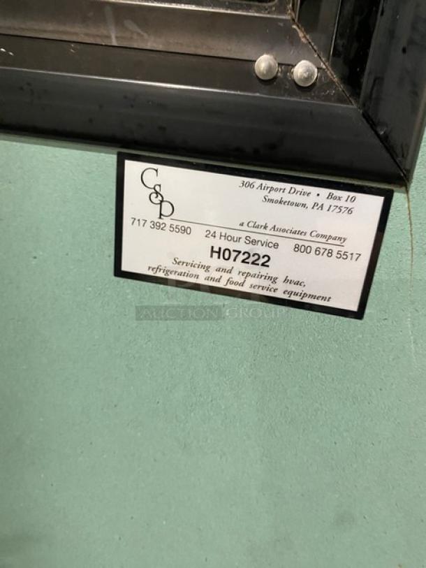 Commercial refrigerated open air multi-tier merchandiser with rear access sliding doors, label indicates service info.