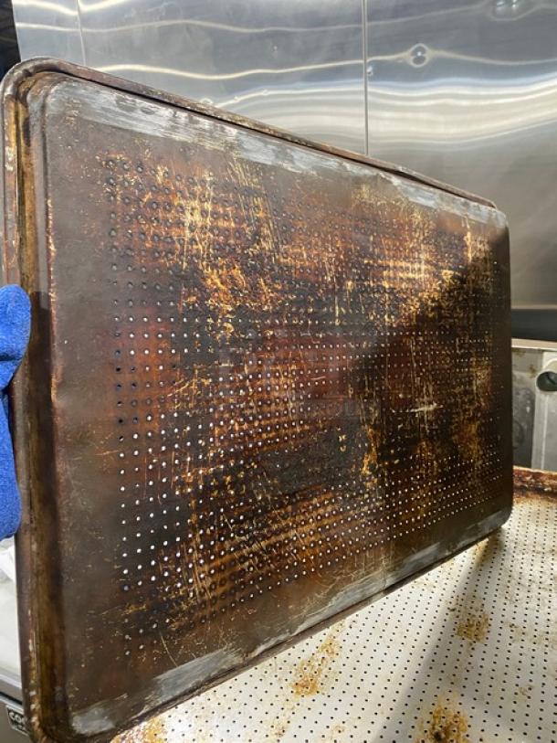 Commercial perforated sheet pan with visible wear and rust, used condition. Great for baking, offers even heat distribution.